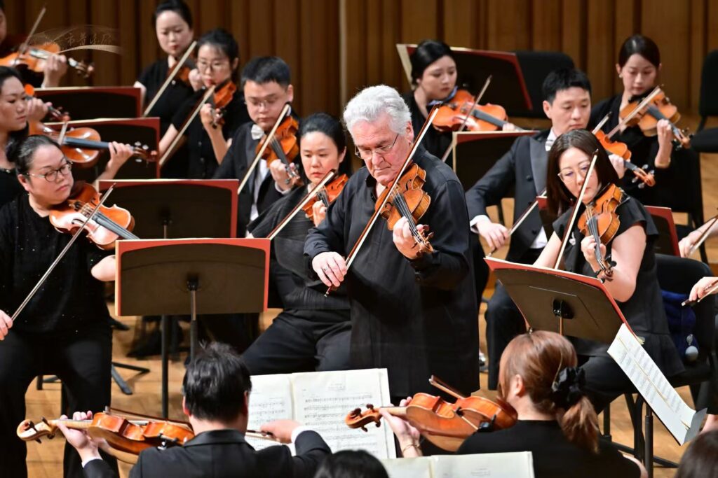 Conductor leads a large string orchestra of violinists on a concert stage